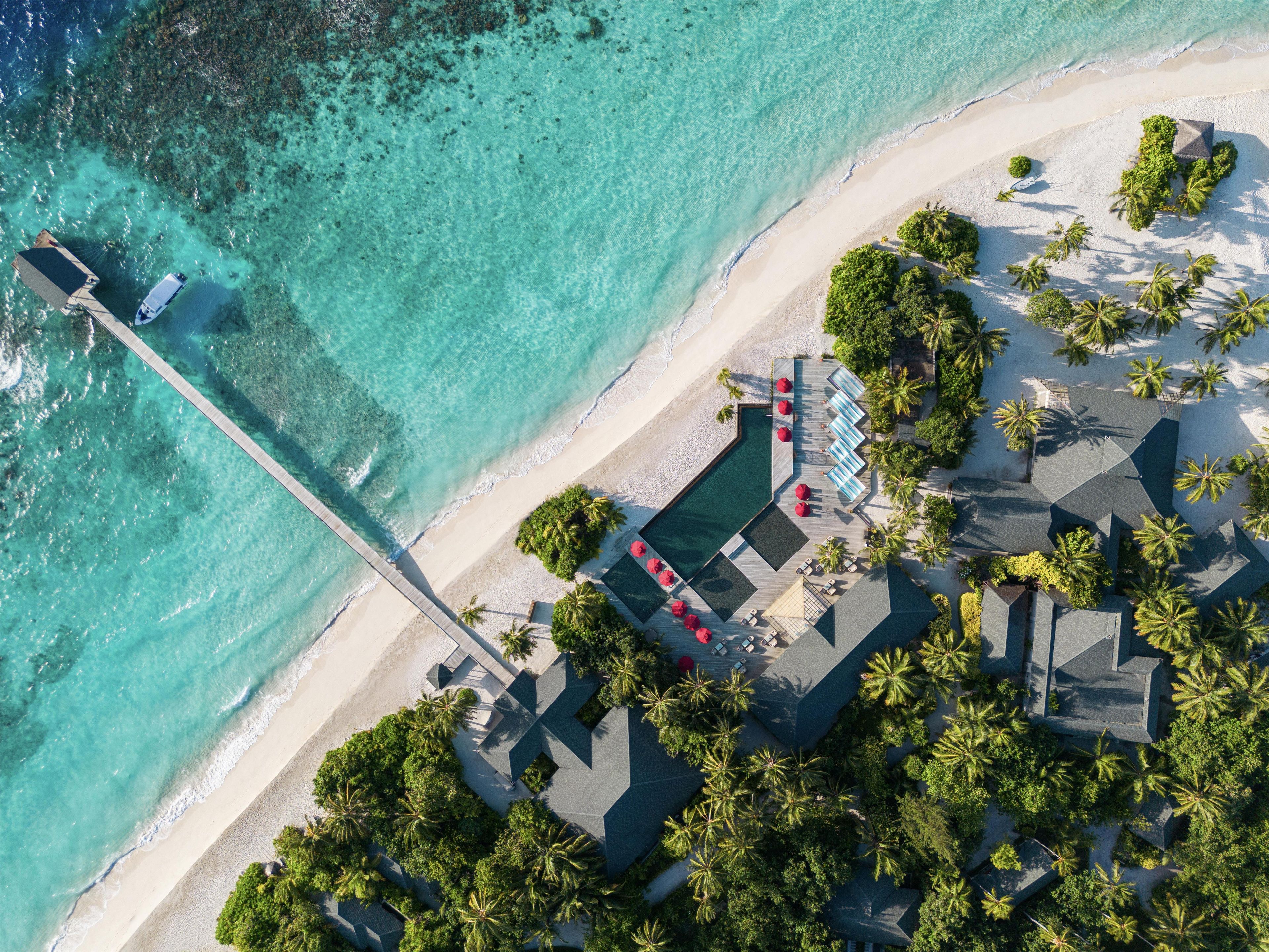 An aerial view of a resort with a pool, lounge chairs, and a pier extending into turquoise waters.