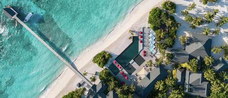 An aerial view of a resort with a pool, lounge chairs, and a pier extending into turquoise waters.