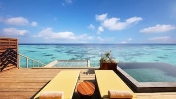 A wooden deck with lounge chairs and a hot tub overlooking a clear blue sea.