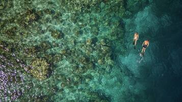 An aerial view of a clear blue water body with coral formations and two people swimming.