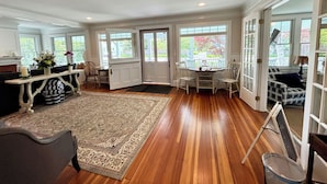 A spacious living room with hardwood flooring, a large rug, a dining area with chairs, and a view through the glass doors.