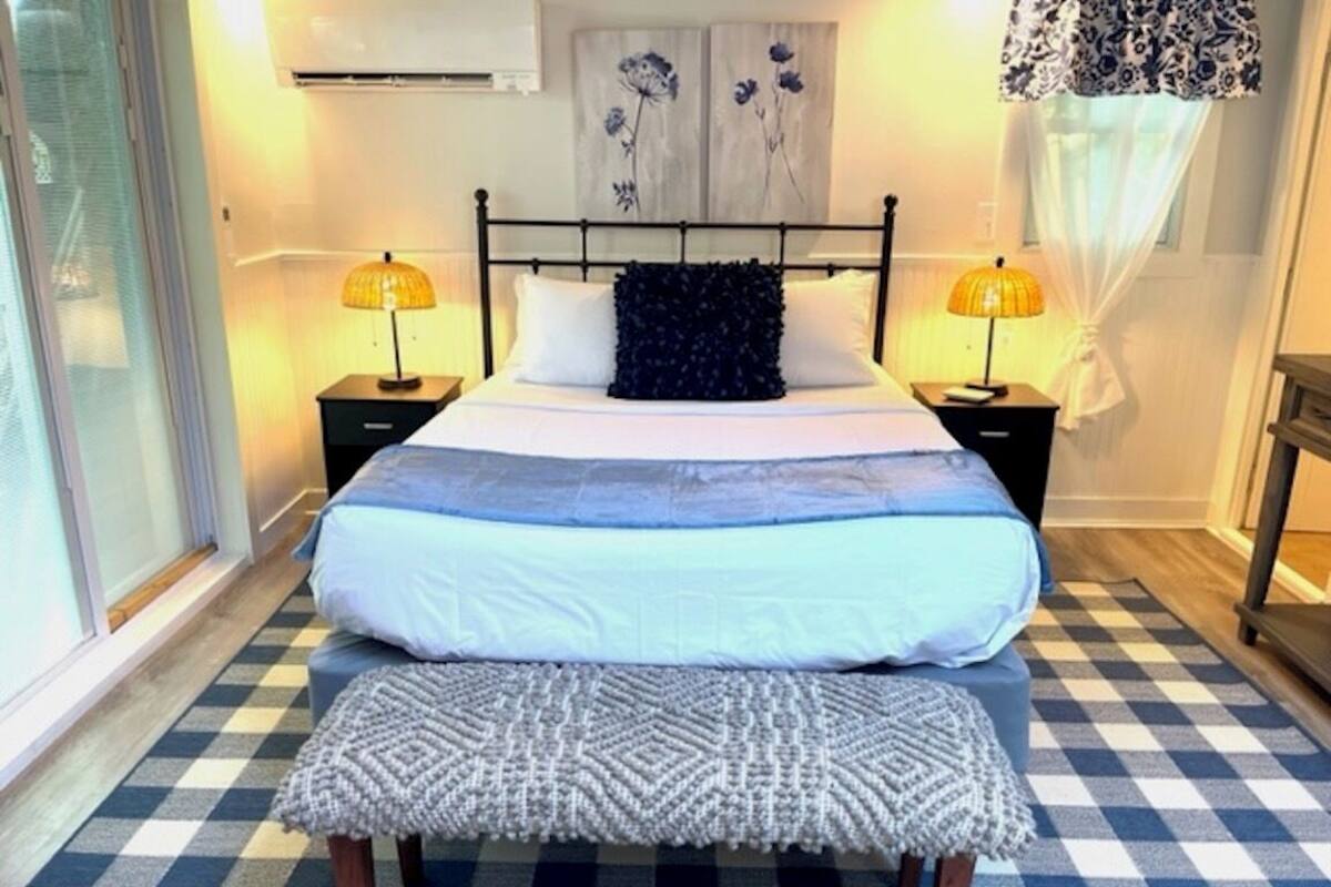 Quarto com uma cama grande, duas mesas de cabeceira com luminárias, piso xadrez e uma janela com cortinas.