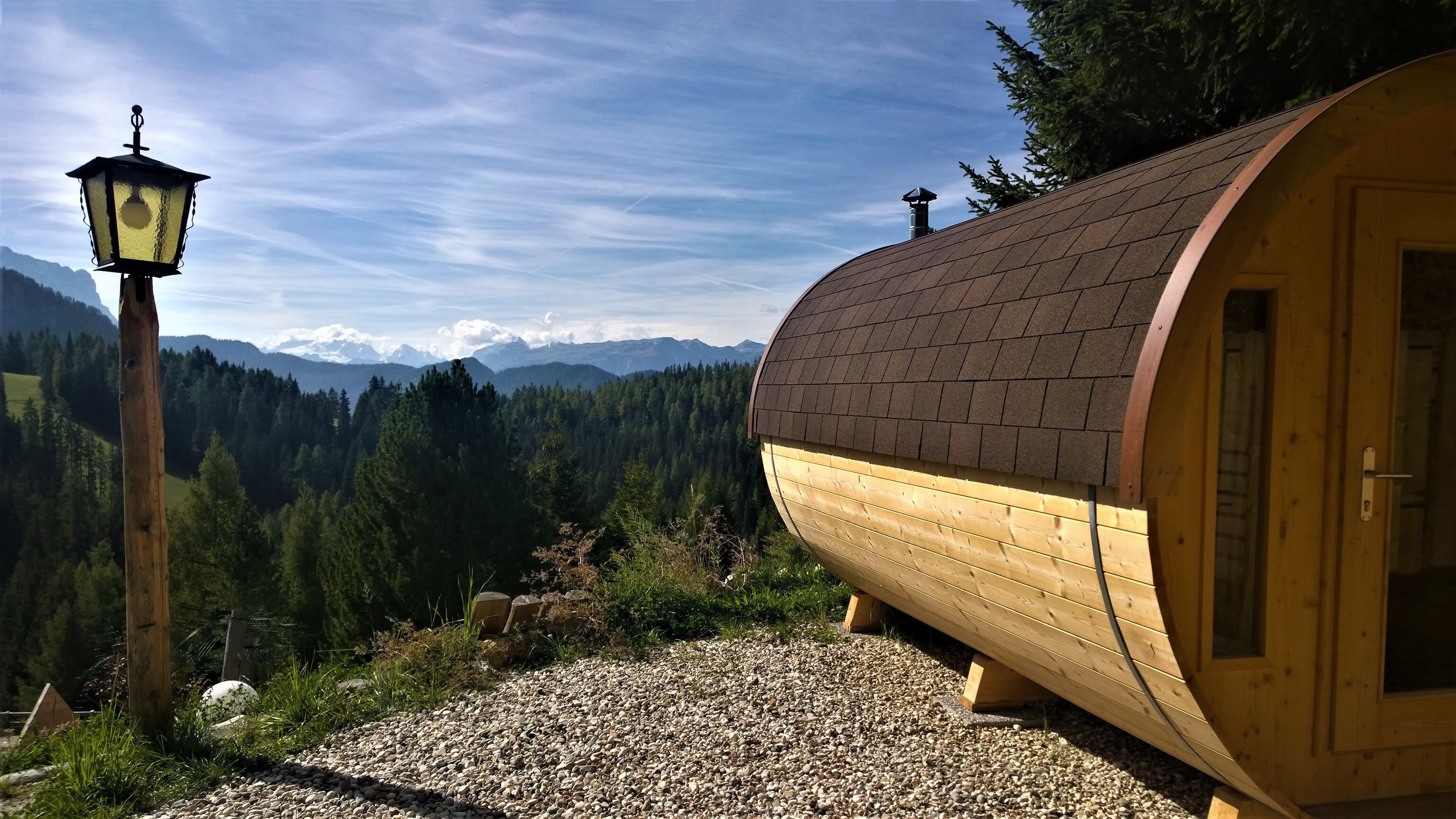 Eine Holzhütte mit geneigtem Dach, einem Kiesweg und einem Berg im Hintergrund.