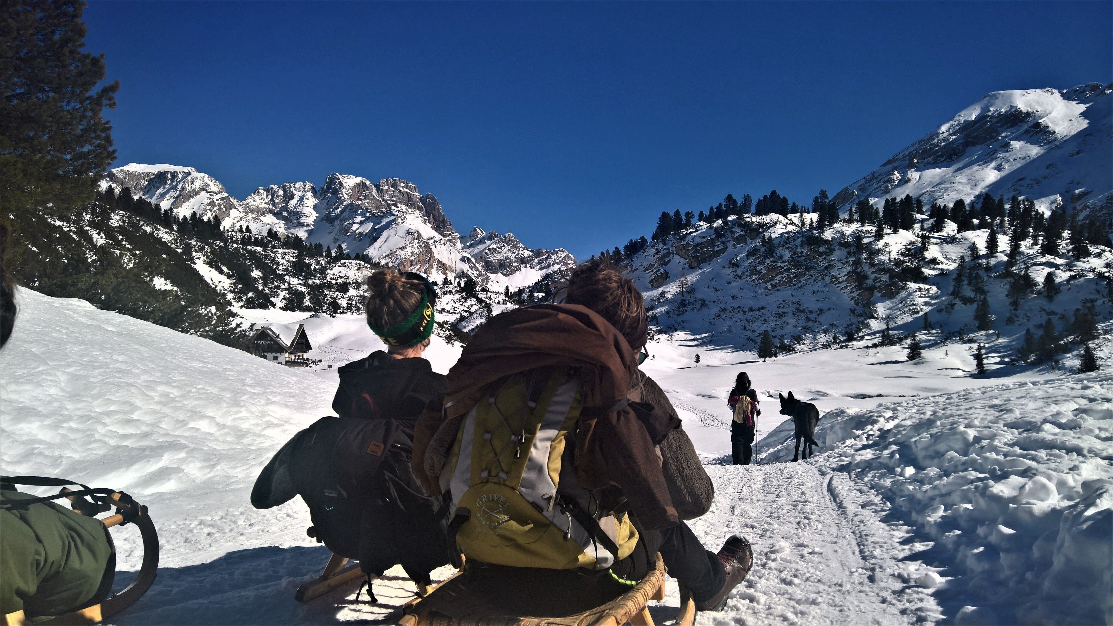 A snowy mountain path with a wooden sled and a person in a green jacket.