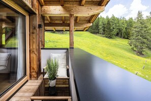 Un balcon avec un banc en bois, un pot de fleurs et une vue sur un paysage verdoyant, parsemé d’arbres.