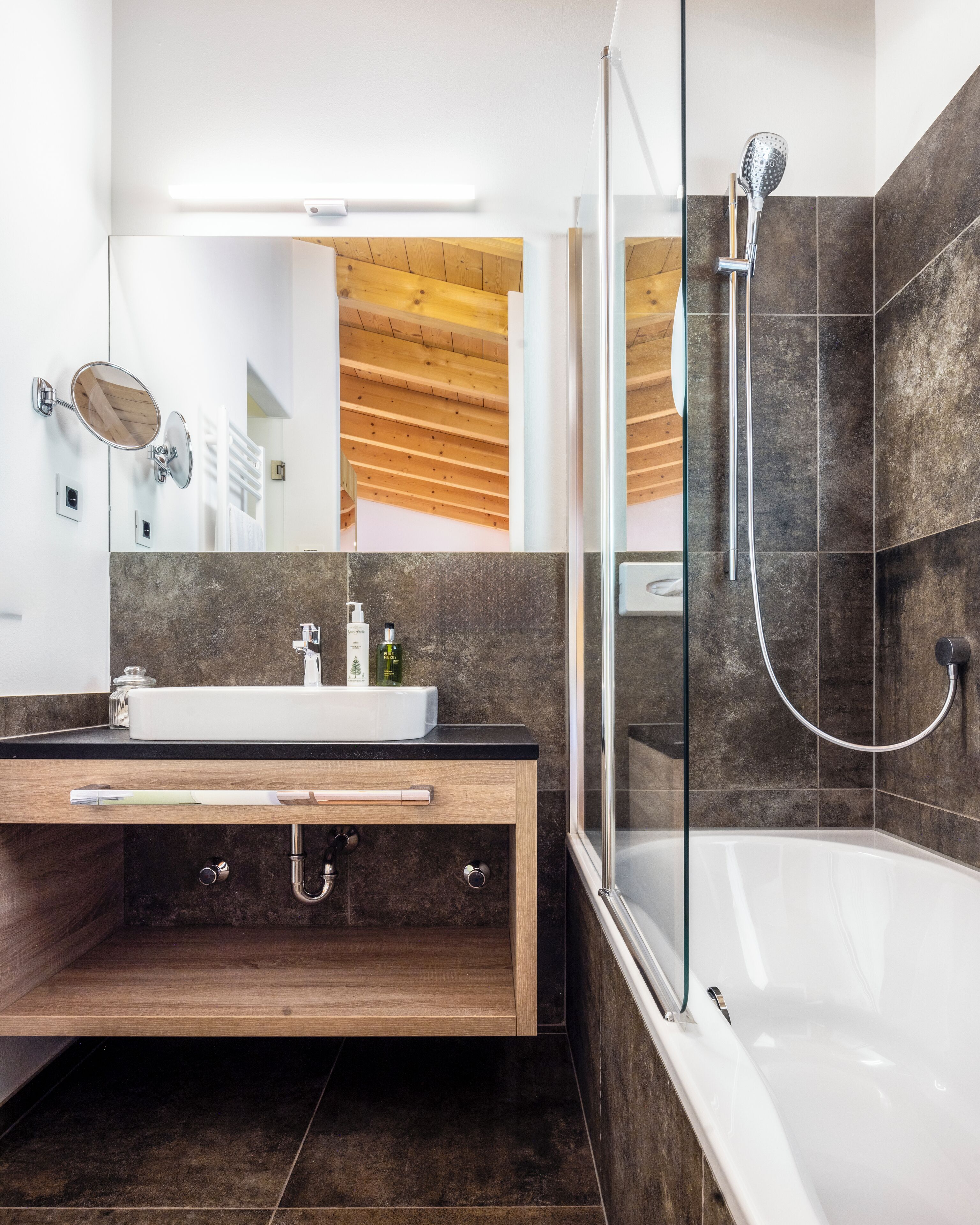 Un baño moderno con ducha de vidrio, tocador de madera con lavamanos y un espejo grande.