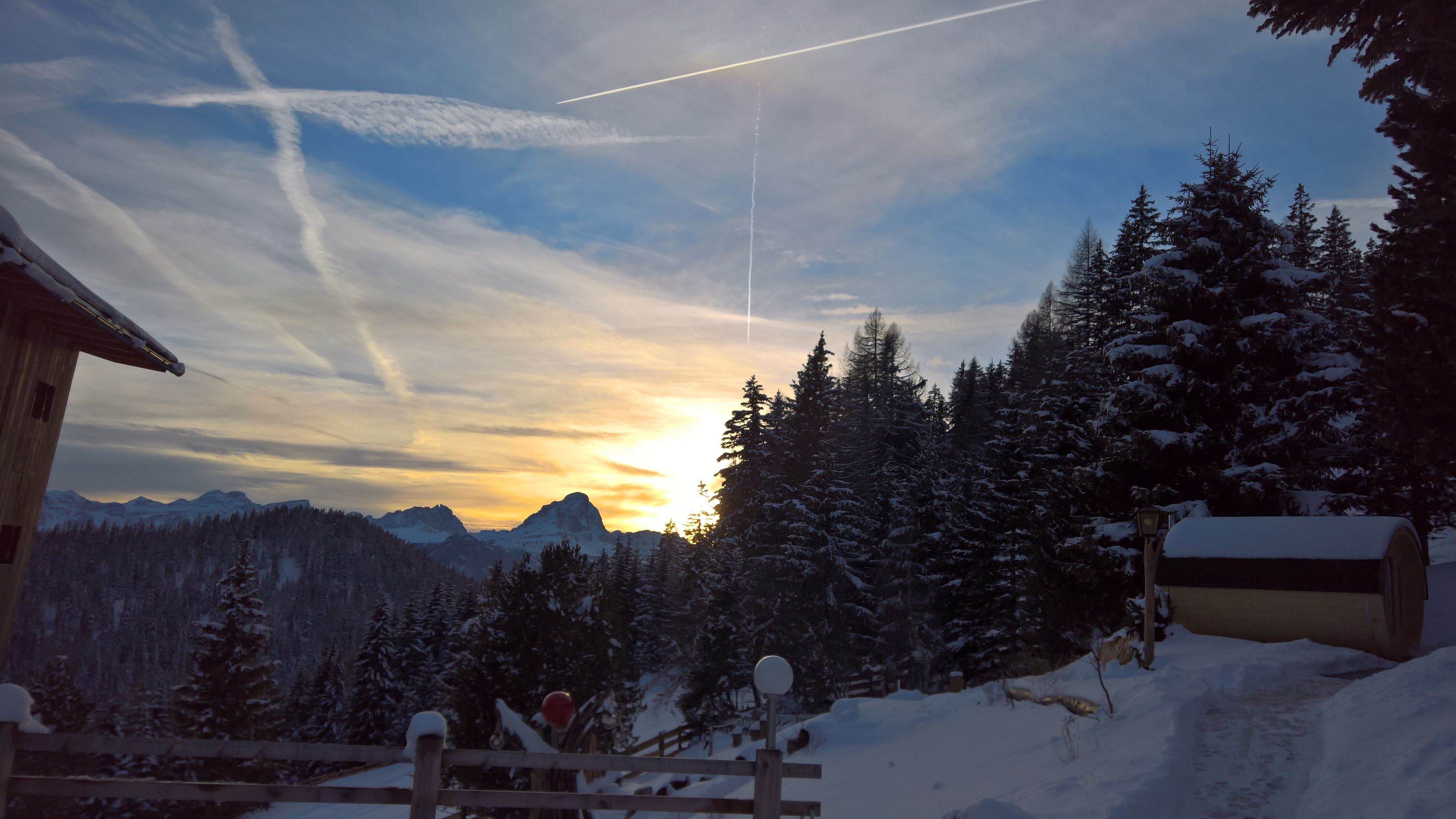 A snowy mountain landscape with a wooden cabin and a snow-covered fence.