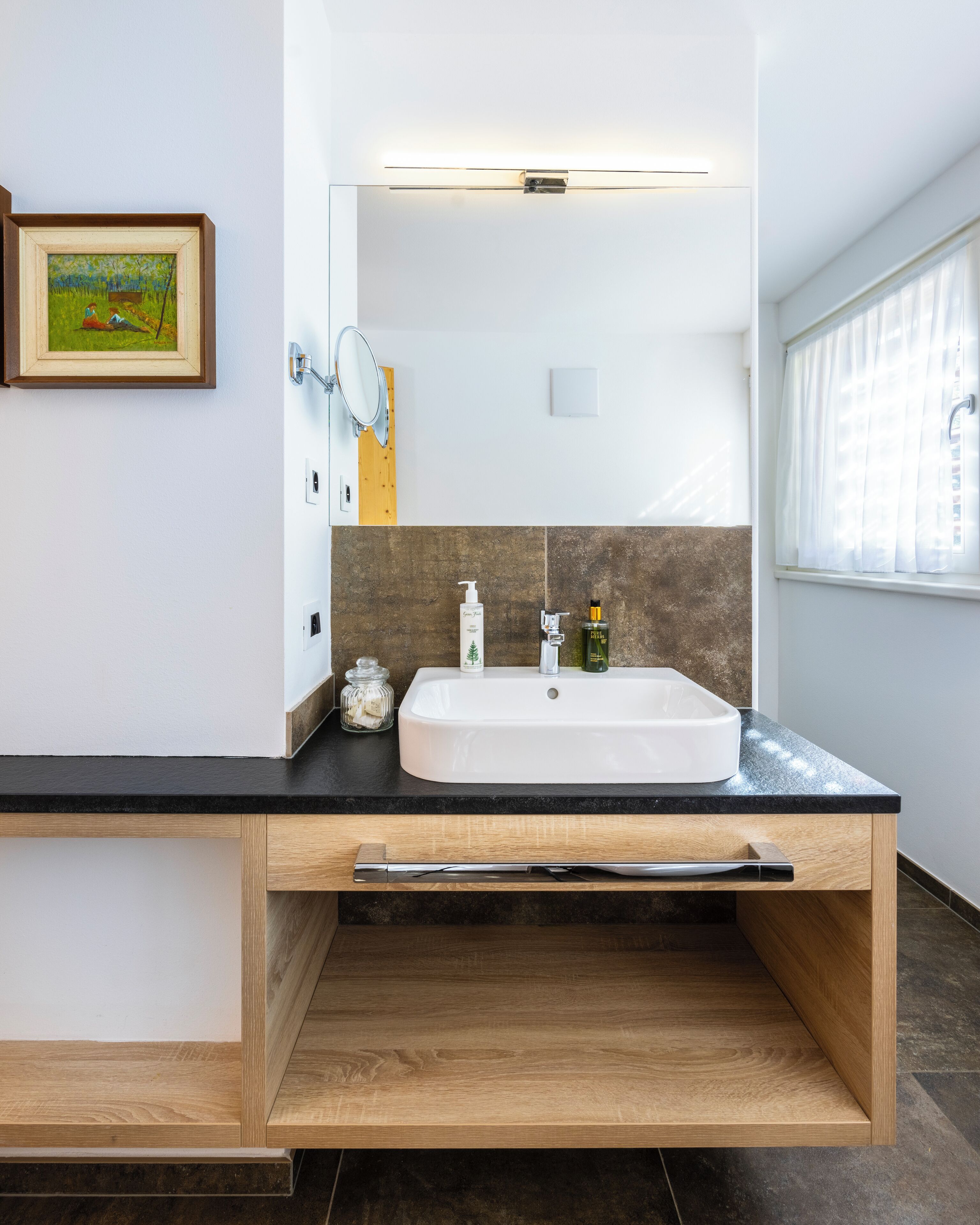 A modern bathroom with a large sink, a mirror, and a window.