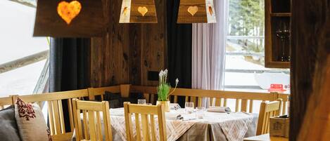 A wooden dining area with a table set for two, benches, and hanging pendant lights with heart-shaped cutouts.