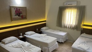 Une chambre d’hôtel avec deux lits simples, une table de chevet, un climatiseur fixé au mur, un tableau et une fenêtre avec des rideaux.