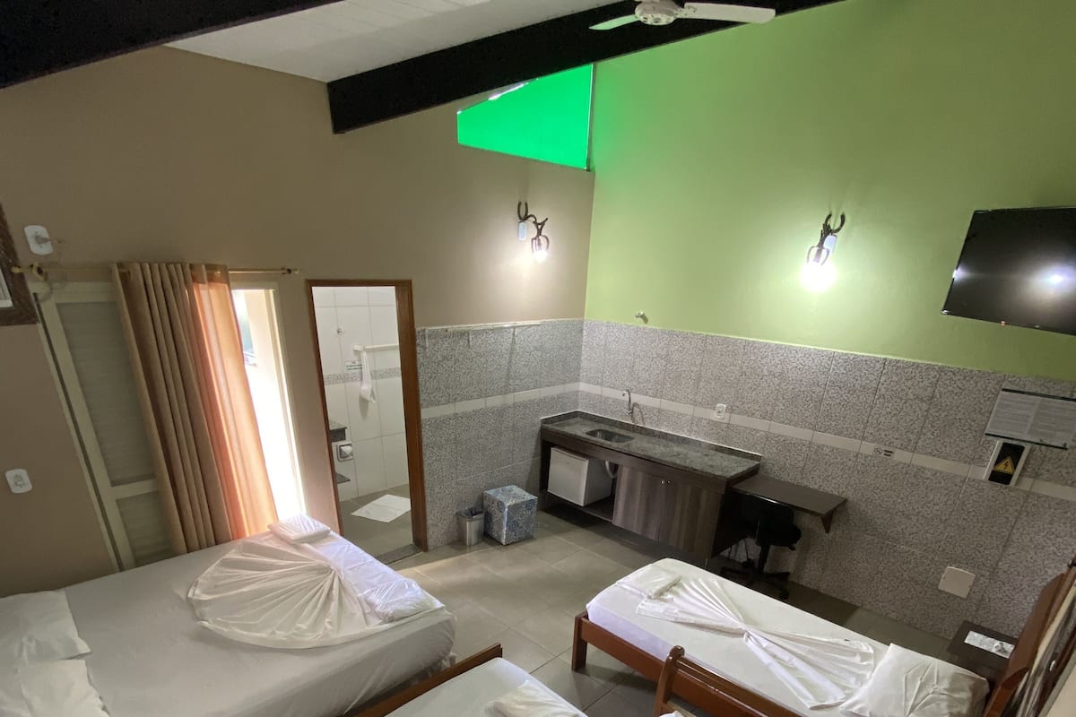 Ett hotellrum med fyra sängar, ett litet kök, ett badrum och en grön vägg.