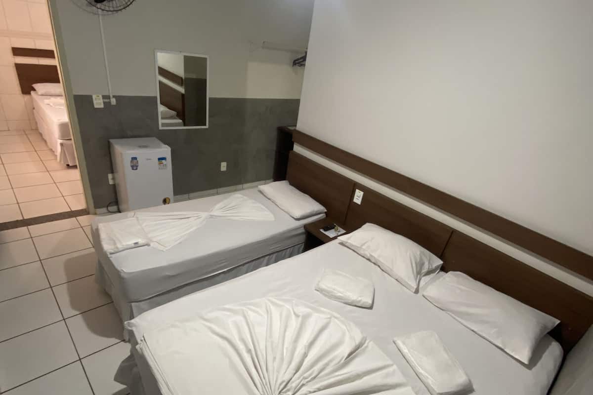 Ett hotellrum med två sängar, ett litet kylskåp, en fläkt som är monterad på väggen och en spegel.