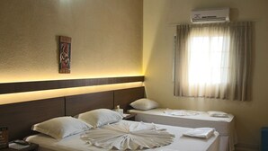 Une chambre d’hôtel avec deux lits, une table de chevet, un climatiseur fixé au mur et une fenêtre avec des rideaux.