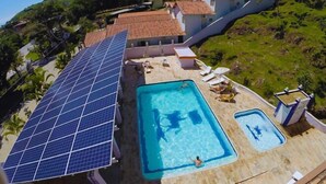 Une piscine sur le toit, dotée de panneaux solaires, de chaises longues et offrant une vue sur le paysage environnant.