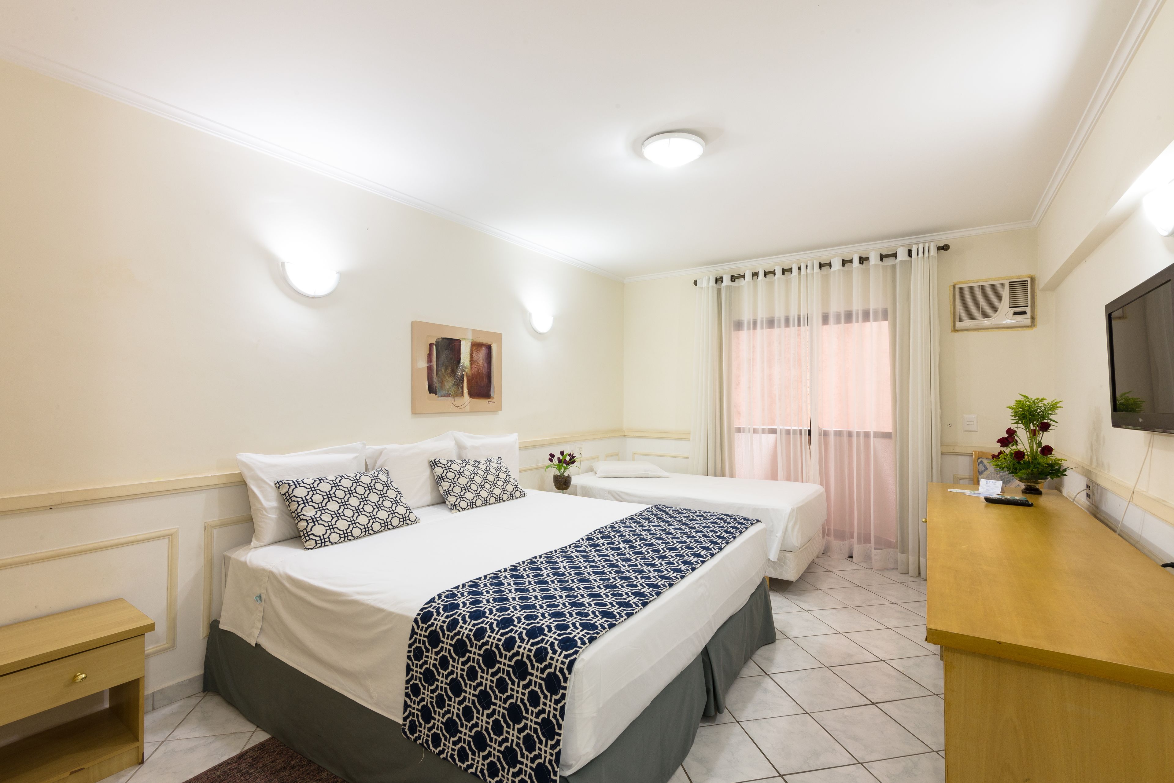A hotel room with two beds, a desk, a TV, and a window with curtains.