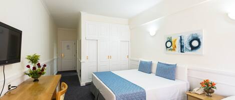 Una habitación de hotel con cama, mesita de noche, televisión y escritorio con silla.