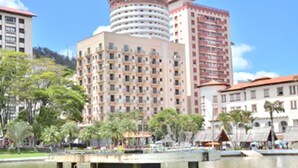 Un hotel de varios pisos con un patio central, una fuente de agua y abundante vegetación alrededor.