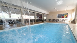 Una piscina interior con fuente acuática, rodeada de sillones de descanso y una zona de bar.