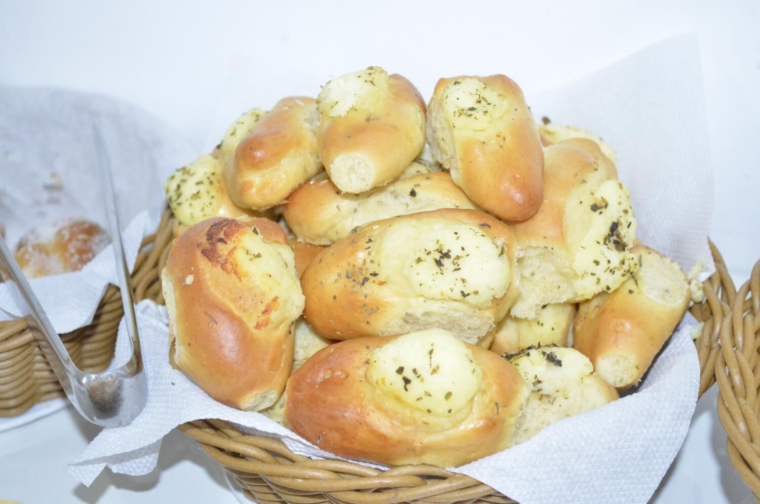 Ein Korb mit frisch gebackenen Brötchen mit Kräutern auf einer weißen Fläche.