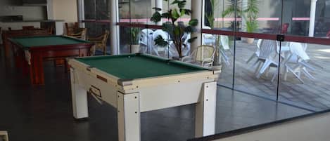 Una mesa de billar en una habitación con vistas a sillas y plantas al aire libre.