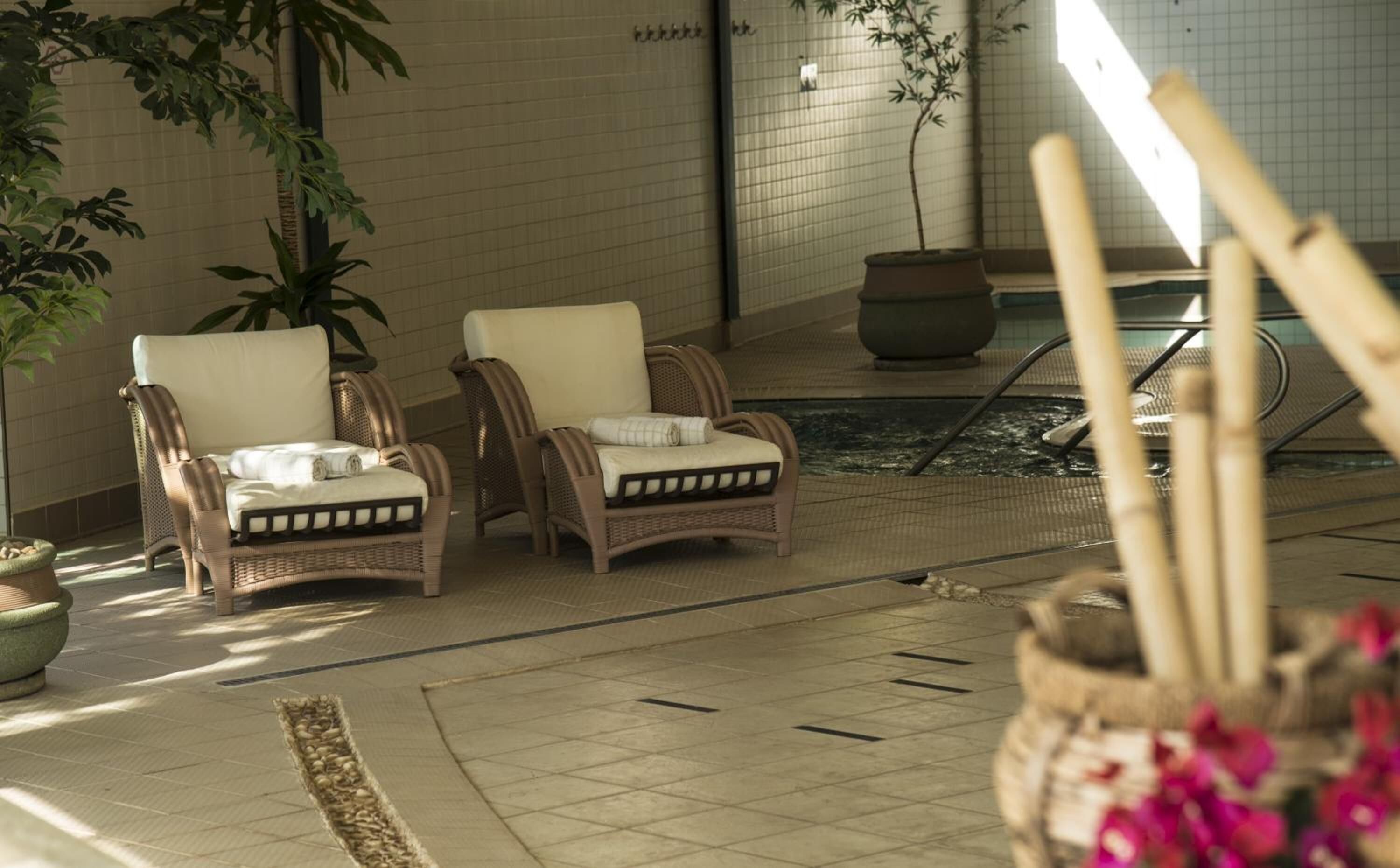 Two wicker lounge chairs with cushions, a tiled floor, a small pool, and potted plants.