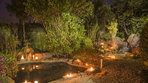Un jardí tranquil amb un estany, un camí de pedra i espelmes.