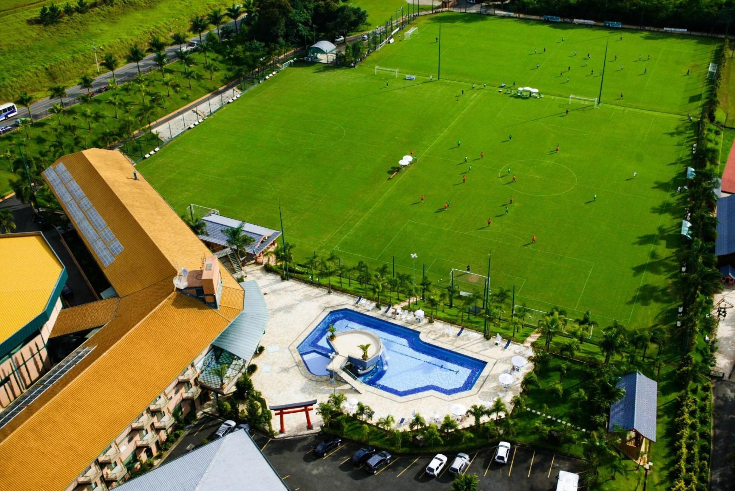Vue aérienne d’un hôtel doté d’une piscine, d’un terrain de football et d’un parking.