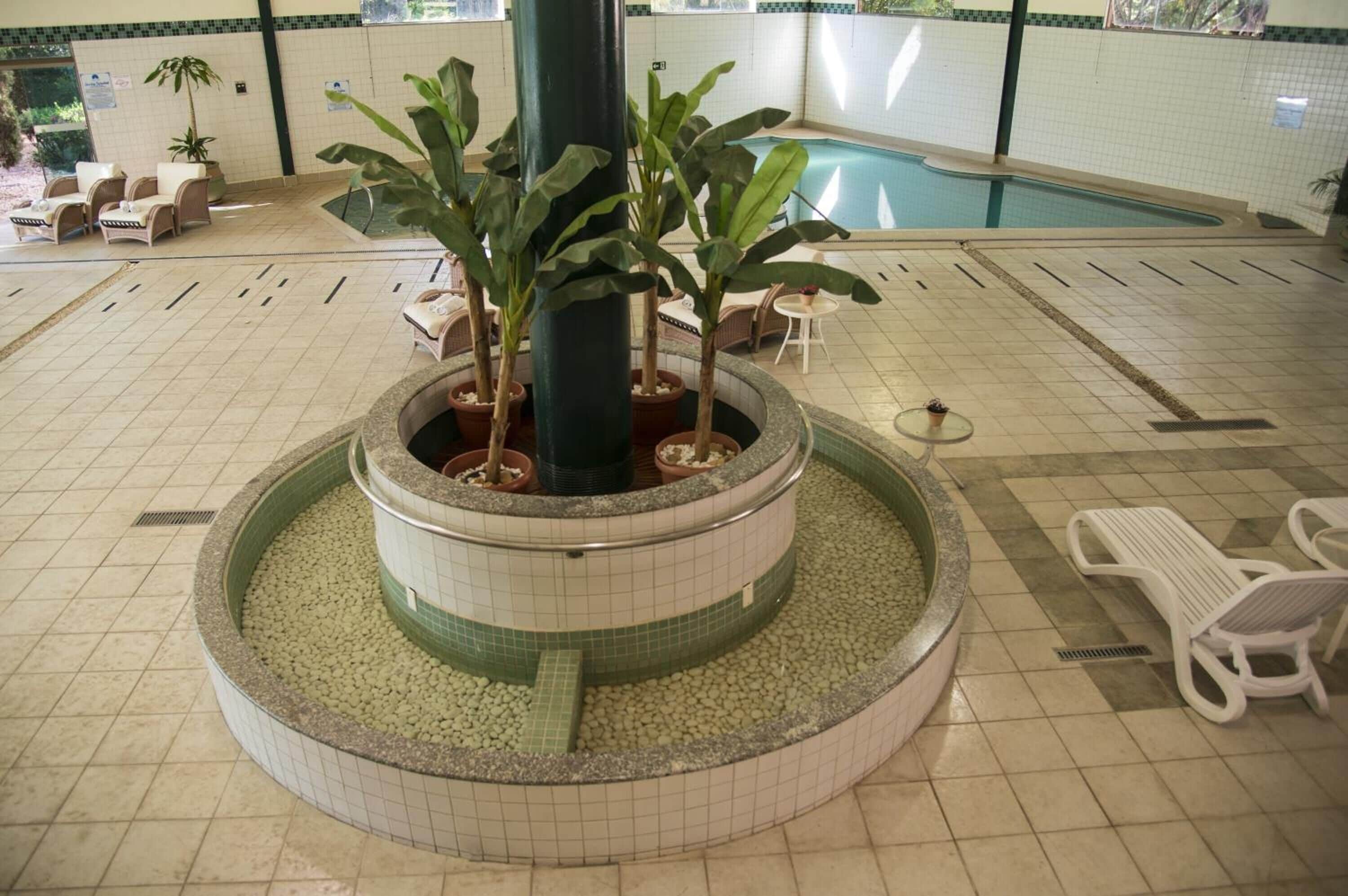 Área interna de piscina com espreguiçadeiras, um elemento central de água e piso revestido de azulejos.