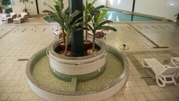 Área interna de piscina com espreguiçadeiras, um elemento central de água e piso revestido de azulejos.