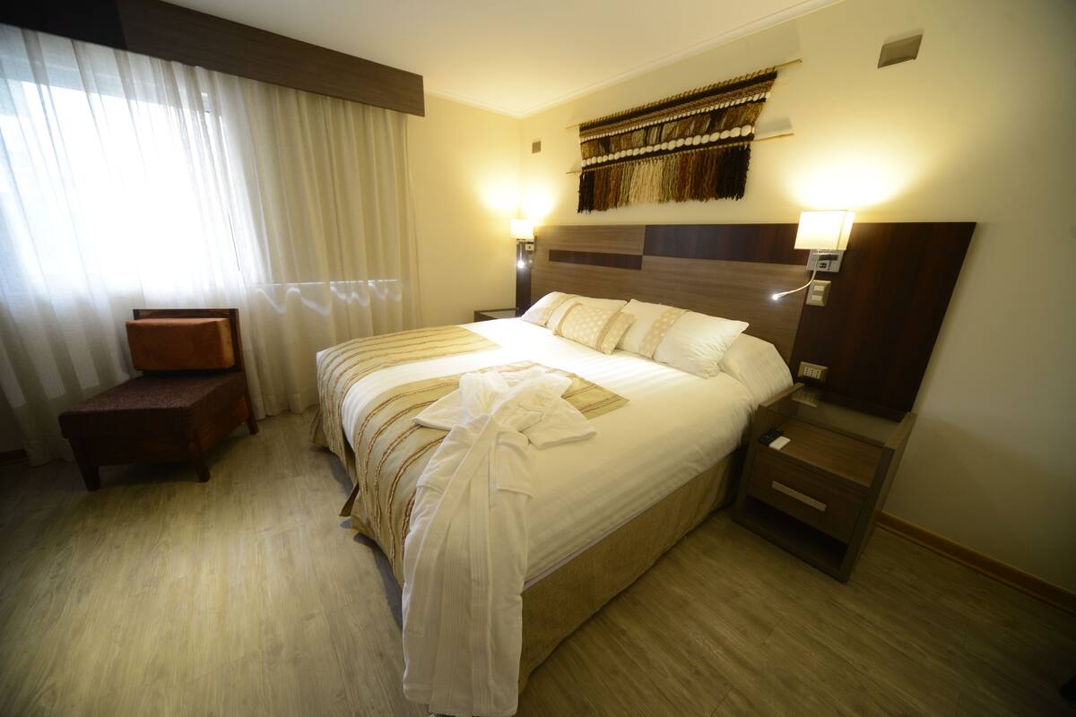 A hotel room with a large bed, a bedside table, a chair, and a wall-mounted TV.