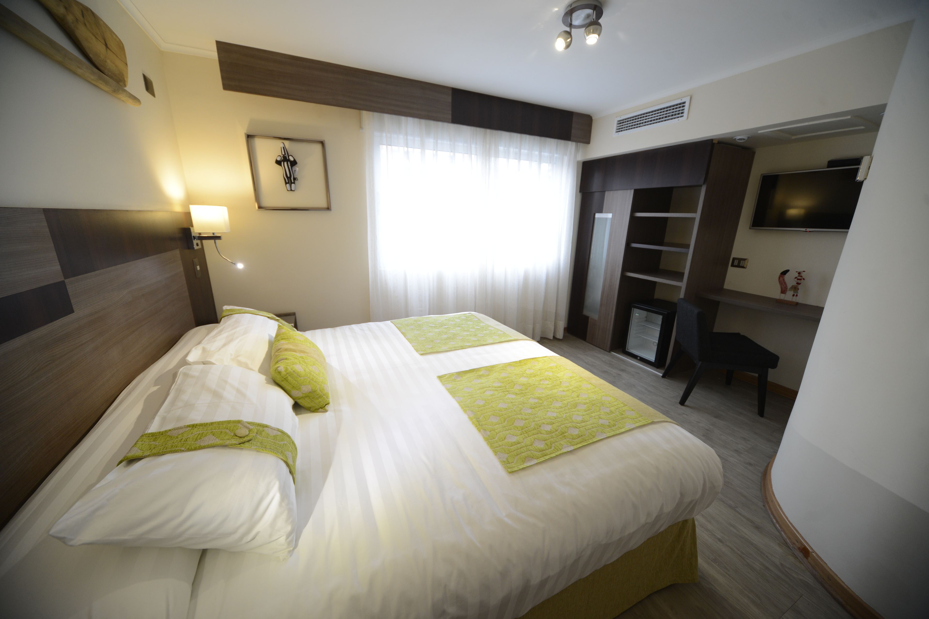 Una habitación de hotel con una cama grande, un escritorio, una silla, un televisor y un armario.