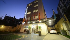 A hotel entrance with a number 2444 sign, flags, and a white car parked outside. - Hotel Boutique Reyall (Santiago)
