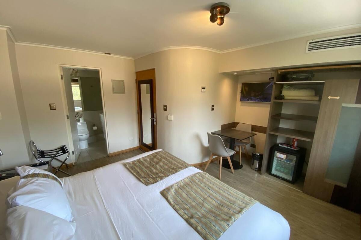 A hotel room with two beds, a desk, a chair, a wardrobe, and a bathroom visible through an open door.