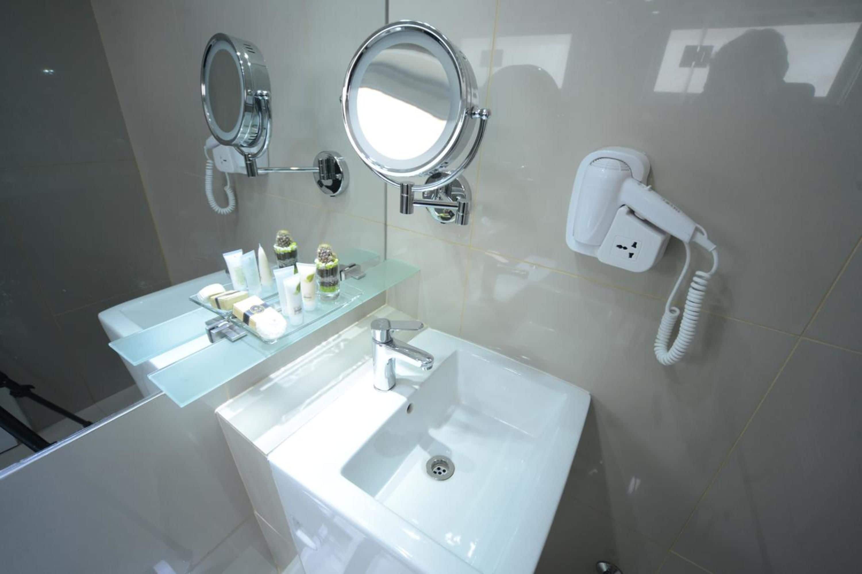 A modern bathroom with a large mirror, a sink, and a hairdryer on the wall.