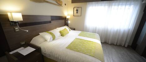 Habitación de hotel con una cama grande, dos mesitas de noche, una lámpara de pared, un cuadro y una ventana con cortinas.