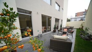 A modern outdoor patio with a wicker sofa, dining table, and chairs. There are potted plants and a small tree with orange fruits. - Hotel Boutique Reyall (Santiago)