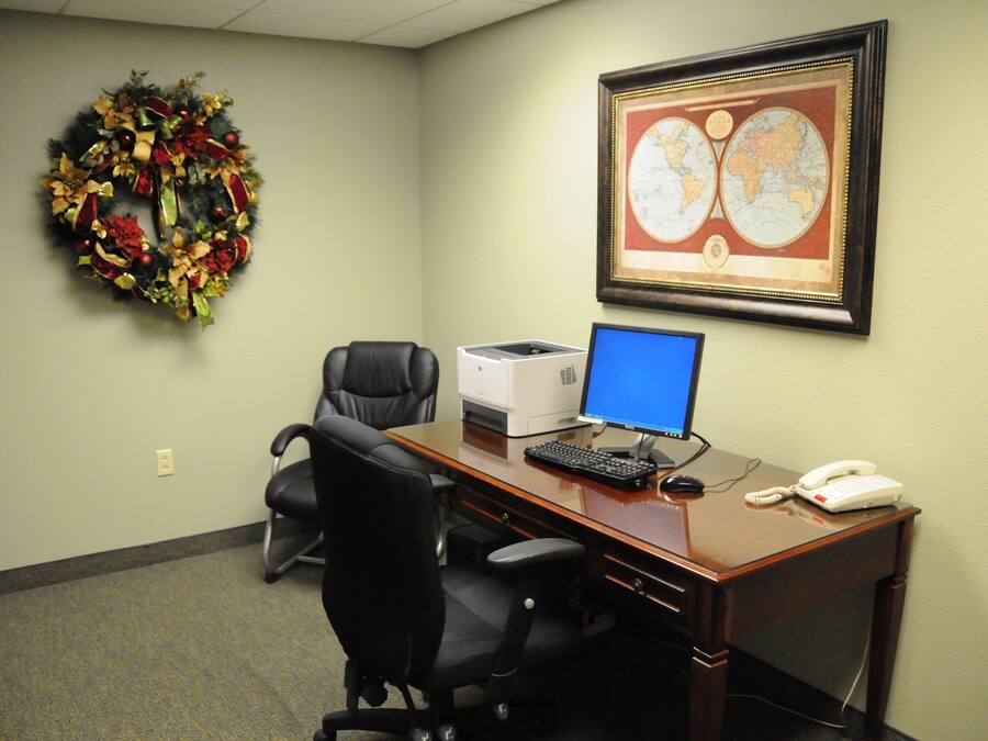 A conference room with a desk, computer, phone, and a framed map on the wall.