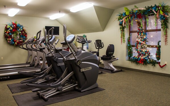 A gym with multiple treadmills and stationary bikes, decorated with Christmas wreaths and ornaments.