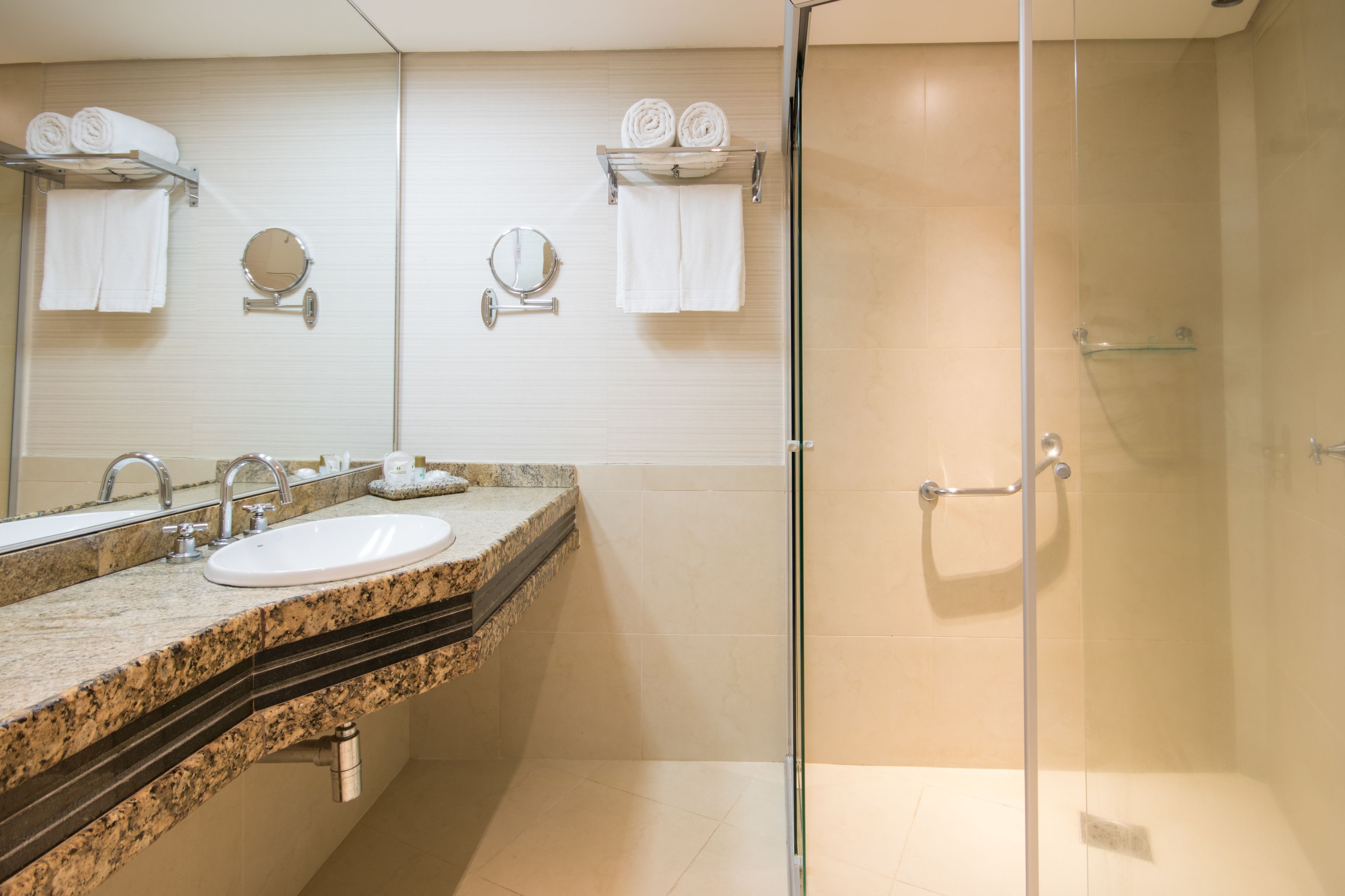A modern bathroom with a granite countertop sink, two mirrors, and a glass-enclosed shower.