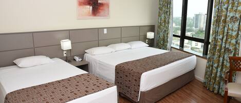 A hotel room with two beds, a nightstand with a phone, a wall-mounted lamp, and a window with curtains.