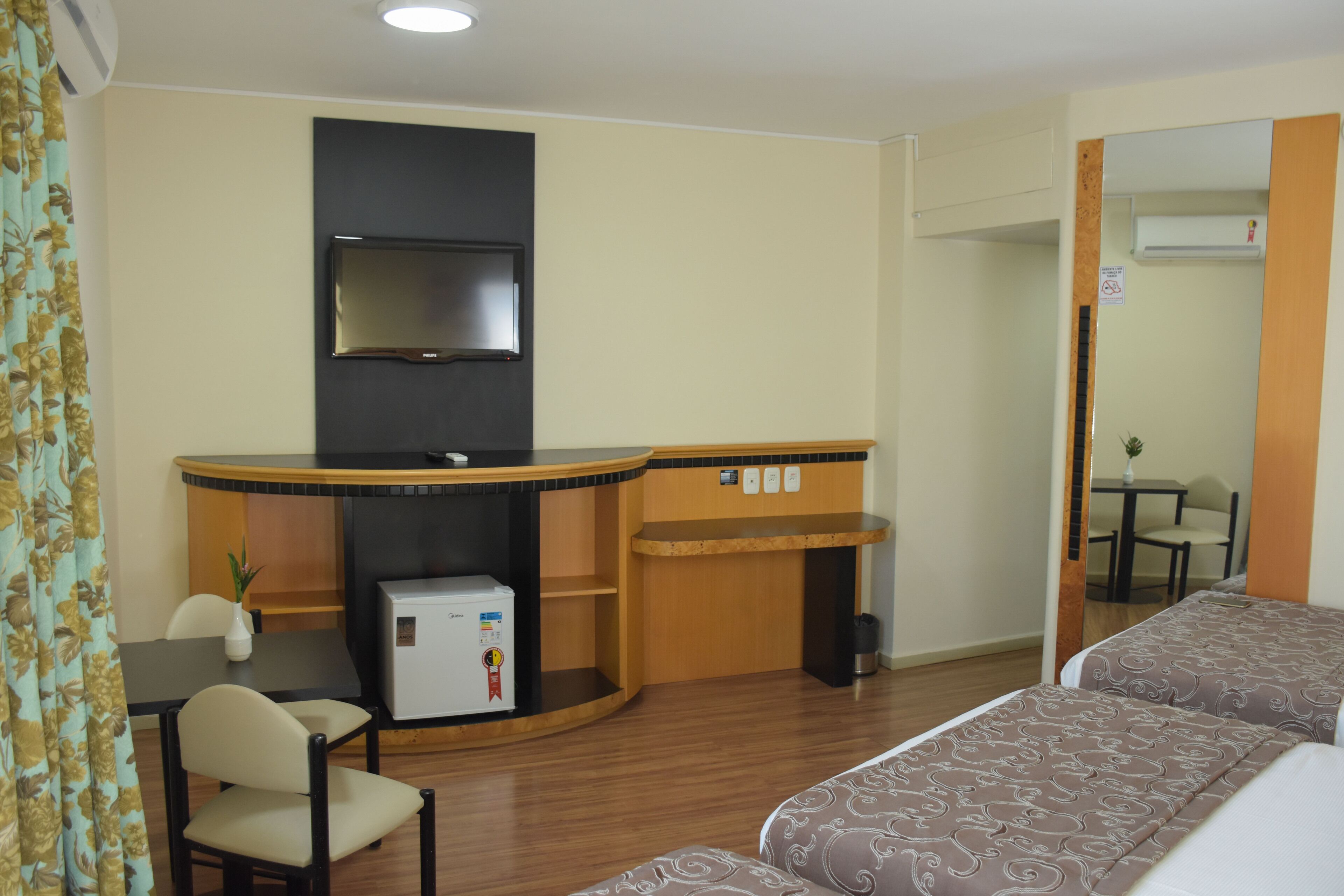 A hotel room with a bed, a desk, a television, and a small refrigerator.