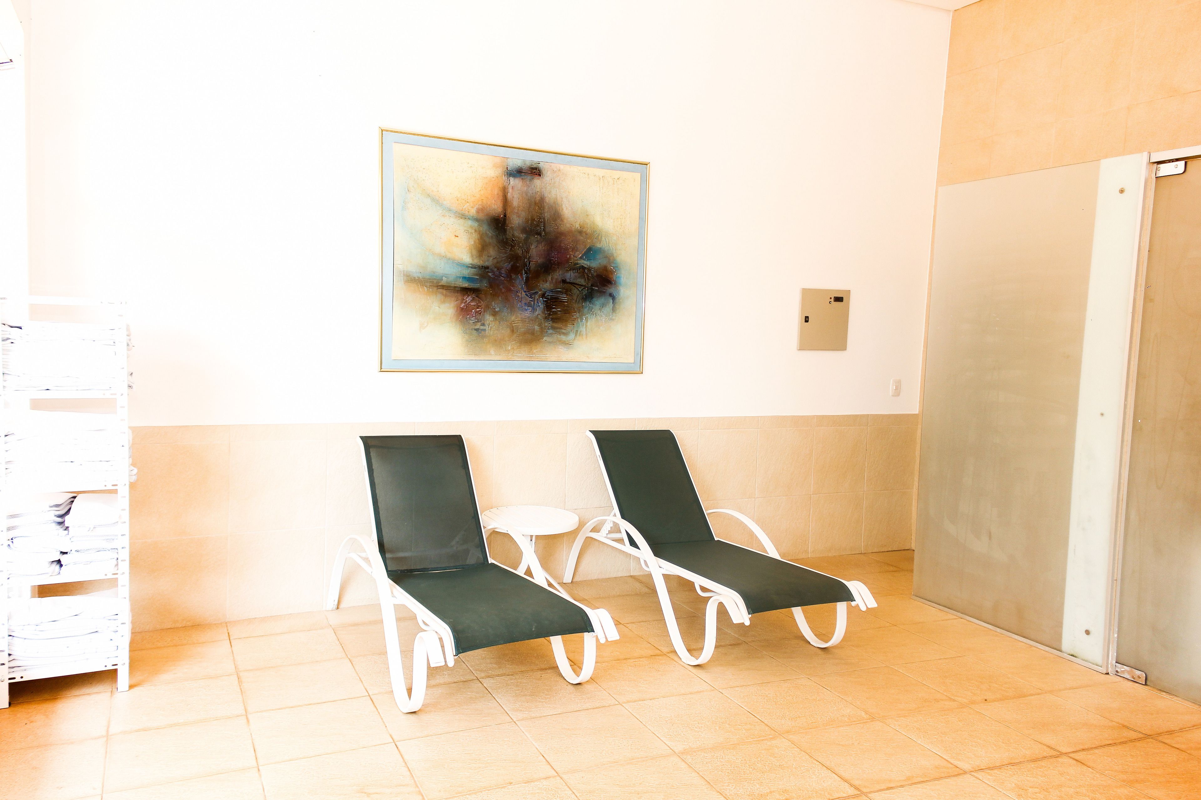 Ein Wartebereich mit zwei Lounge-Sesseln, einem kleinen Tisch, einem an der Wand befestigten abstrakten Gemälde und einem Fliesenboden.