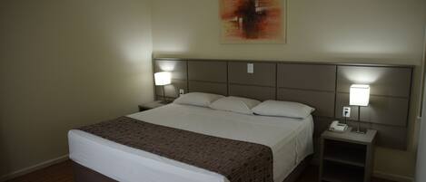 Une chambre d’hôtel avec un grand lit, deux tables de chevet avec des lampes, un climatiseur fixé au mur et un tableau au-dessus du lit.
