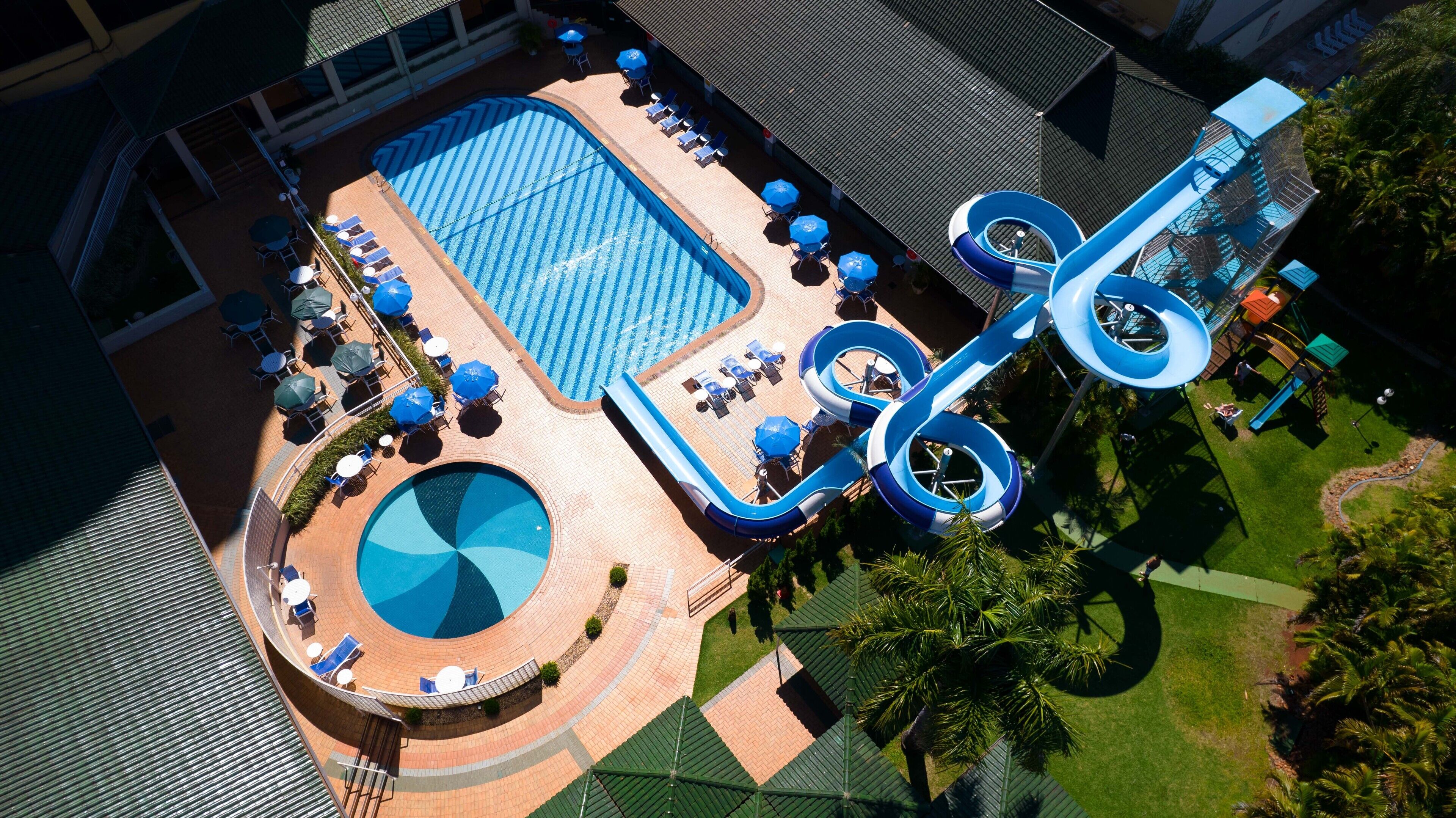 Vista aérea de un resort con una gran piscina, un tobogán de agua y una piscina circular.