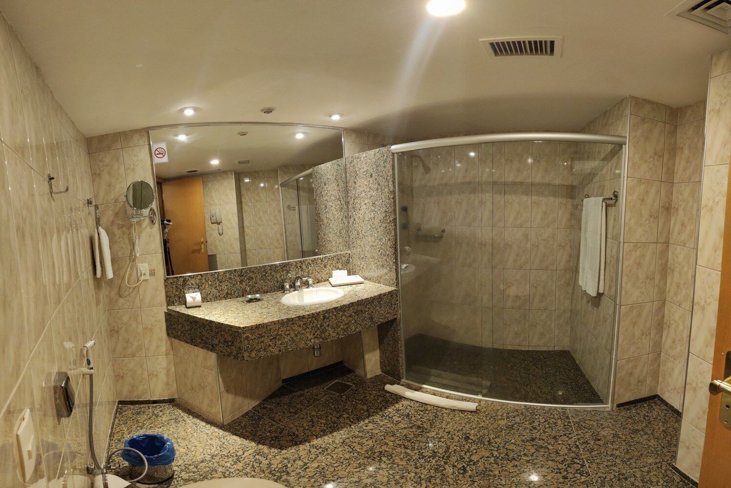 A modern bathroom with a granite countertop sink, a glass shower enclosure, and a large mirror.