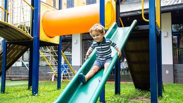 A child on a green slide at a playground with yellow and blue structures.