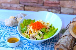 Un tazón de ensalada con zanahorias ralladas y champiñones sobre un plato blanco, colocado sobre una mesa con mantel azul.