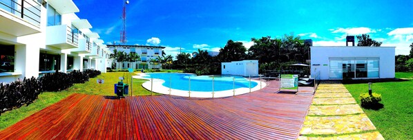 Un hotel moderno con piscina, terraza cubierta y césped bien cuidado.