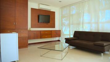 A modern living room with a glass coffee table, brown sofa, wooden cabinets, and a flat-screen TV mounted on the wall.
