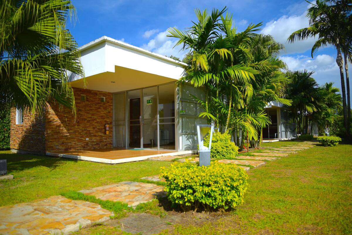 A modern building with a glass entrance, surrounded by lush greenery and palm trees.